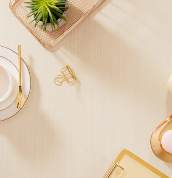 Modern gold stylized home office desk with folder, macaroons, coffee mug on beige background. Flat lay, top view lifestyle concept.